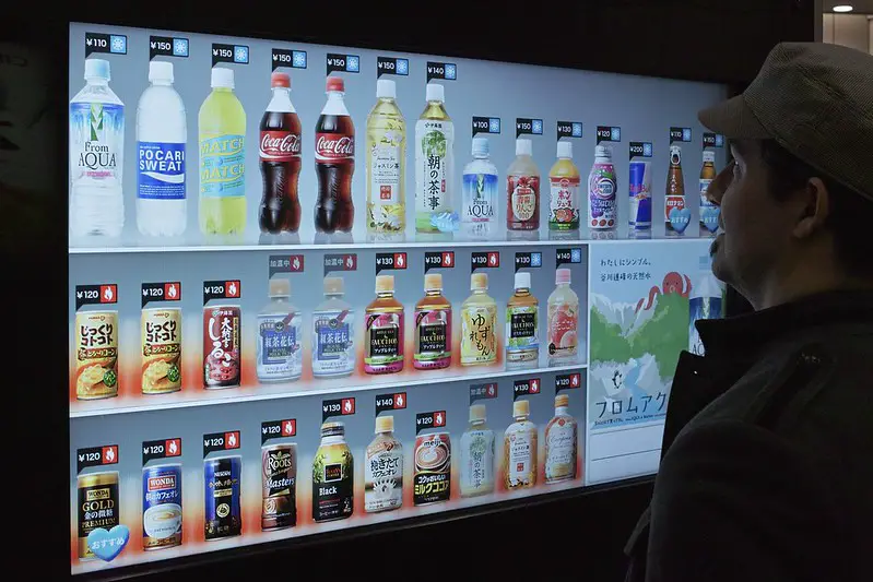 A man standing in front of a vending machine that recommends drinks
